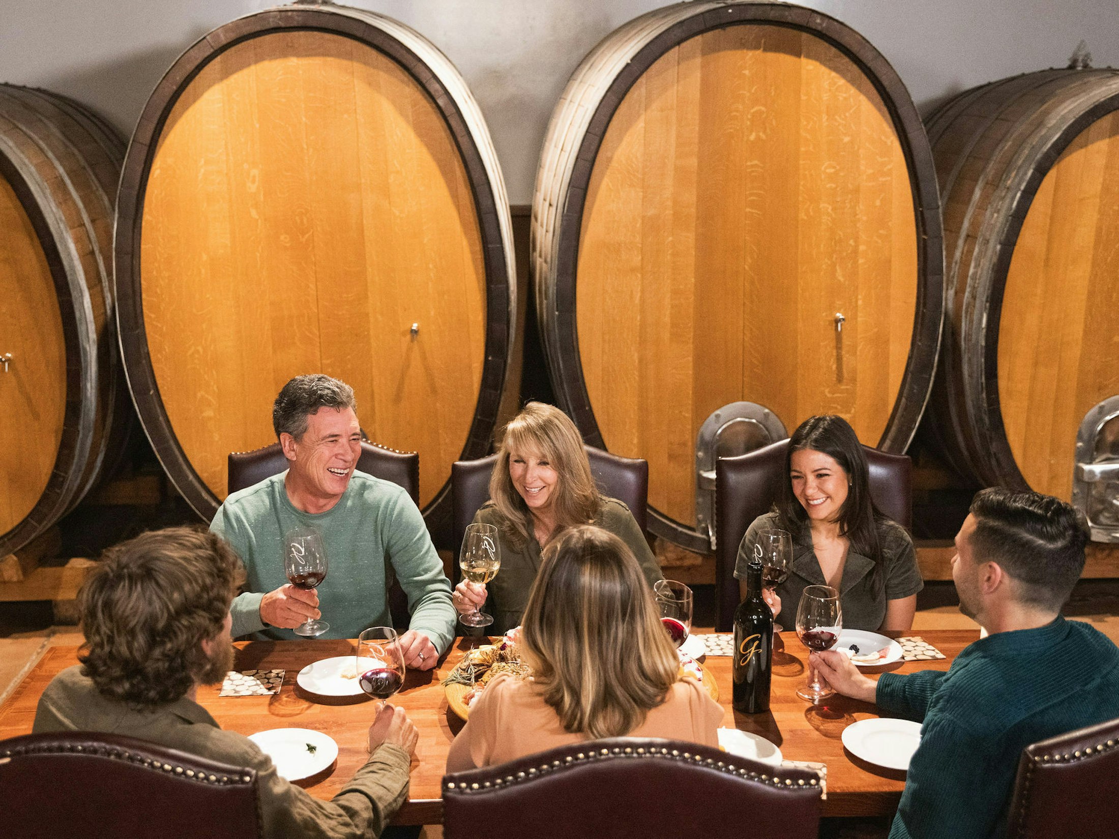 People happily drinking wine in front of large wine barrels