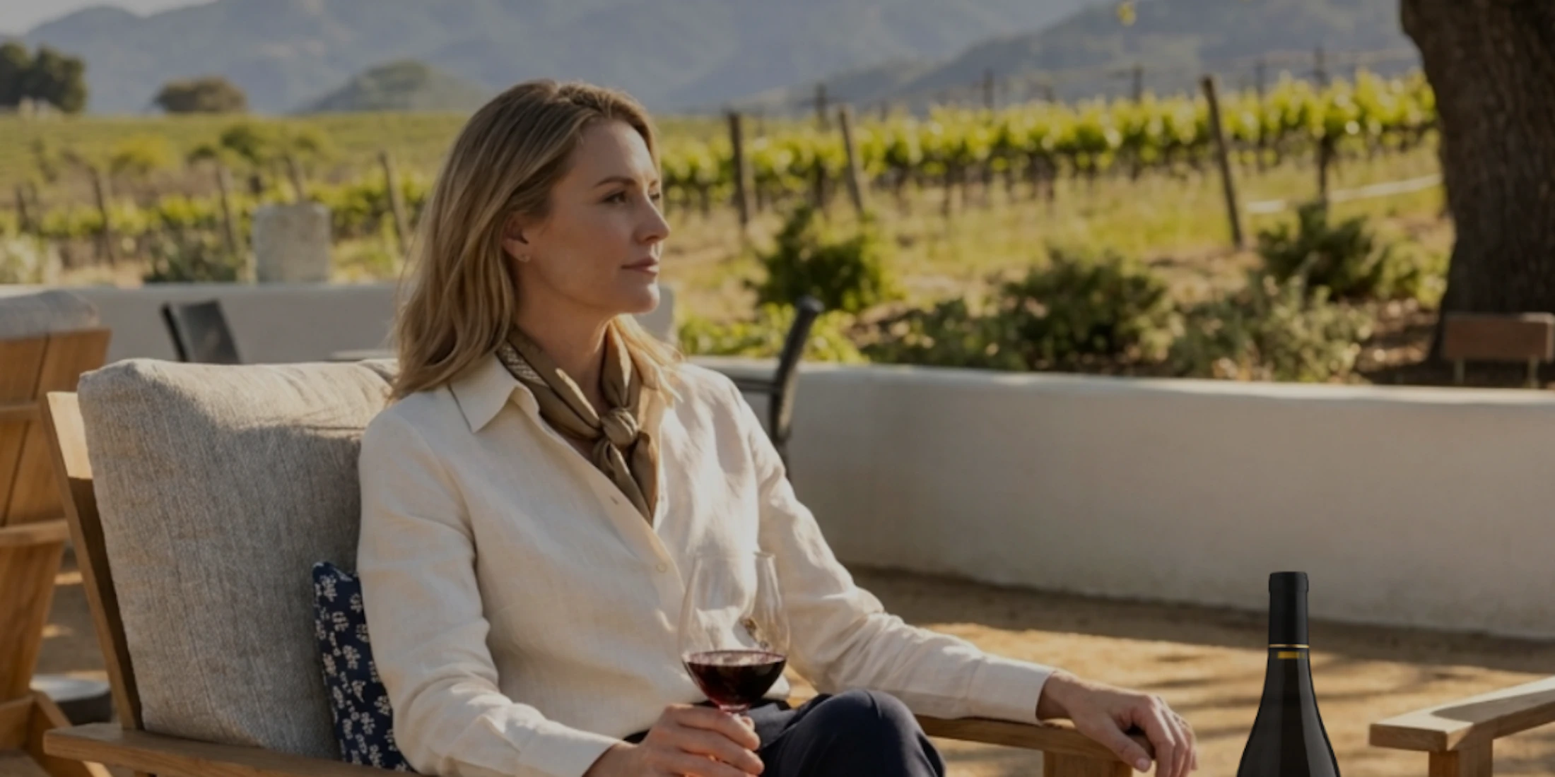 woman with a bottle of wine sitting at a table at a vineyard